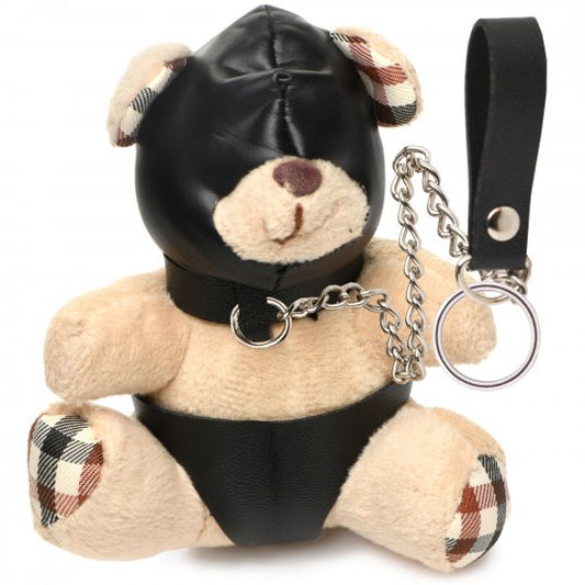 A small beige bear with light peach fur, dressed in PU leather panties and a hood, wearing a gimp mask, and attached to a collar with a metal chain leash, positioned on a white background.