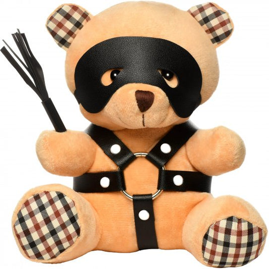 A cute bondage-themed stuffed bear with light peach fur, wearing a faux leather harness with metal O-rings, holding a mini flogger, and featuring a removable eye mask, measuring 8.5 inches in length, 6.5 inches in width, and 5.5 inches in depth.