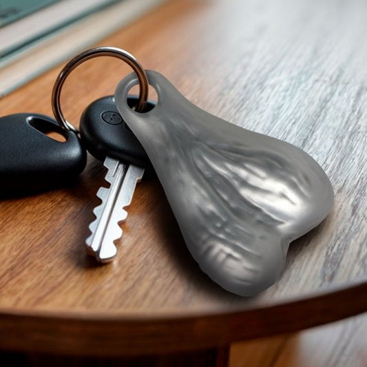 A humorous keychain featuring large plastic testicles hanging from a nickel-free metal ring, set against a neutral background.