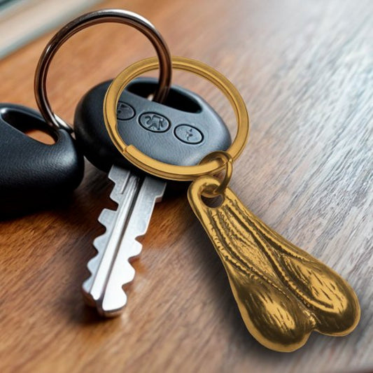 A humorous keychain featuring oversized brass testicles hanging from a nickel-free metal ring, designed to be a fun accessory for keys or bags.