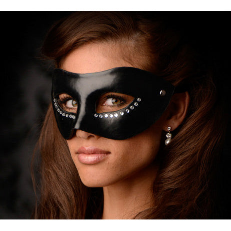 A black Venetian style mask with crystal accents around the eyes, made of faux leather and plastic, secured with long satin ties, resting against a background that suggests a sense of mystery and elegance.