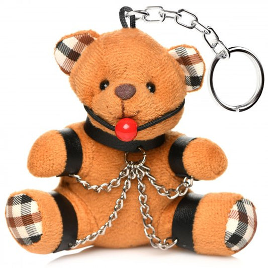 A small brown teddy bear with a ball gag in its mouth, bound with collar, wrist and ankle cuffs, and nickel-free chains, designed as a gag gift and keychain accessory, positioned against a plain background.